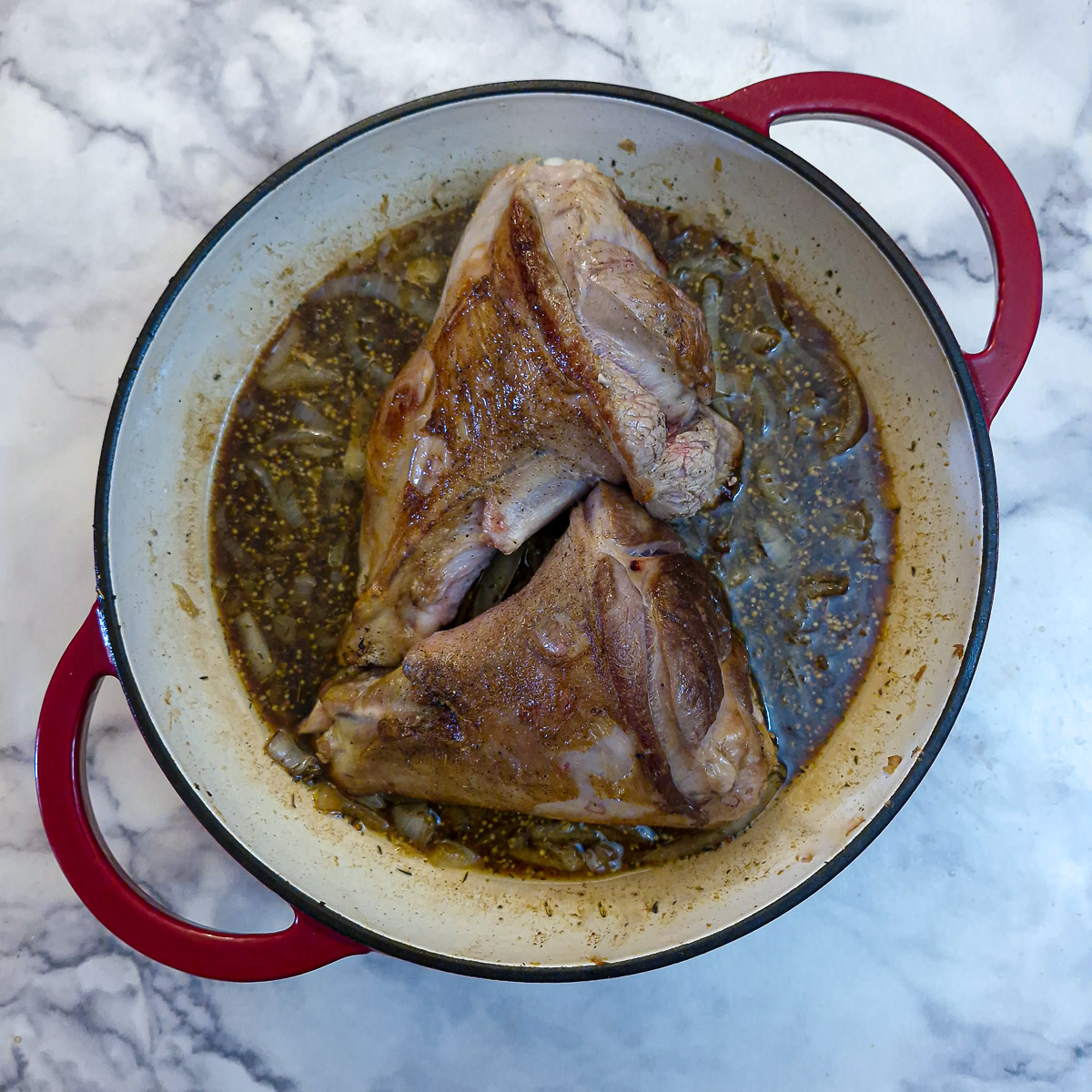 Step 3 - add the gravy to the pan and place the lamb shanks on top.