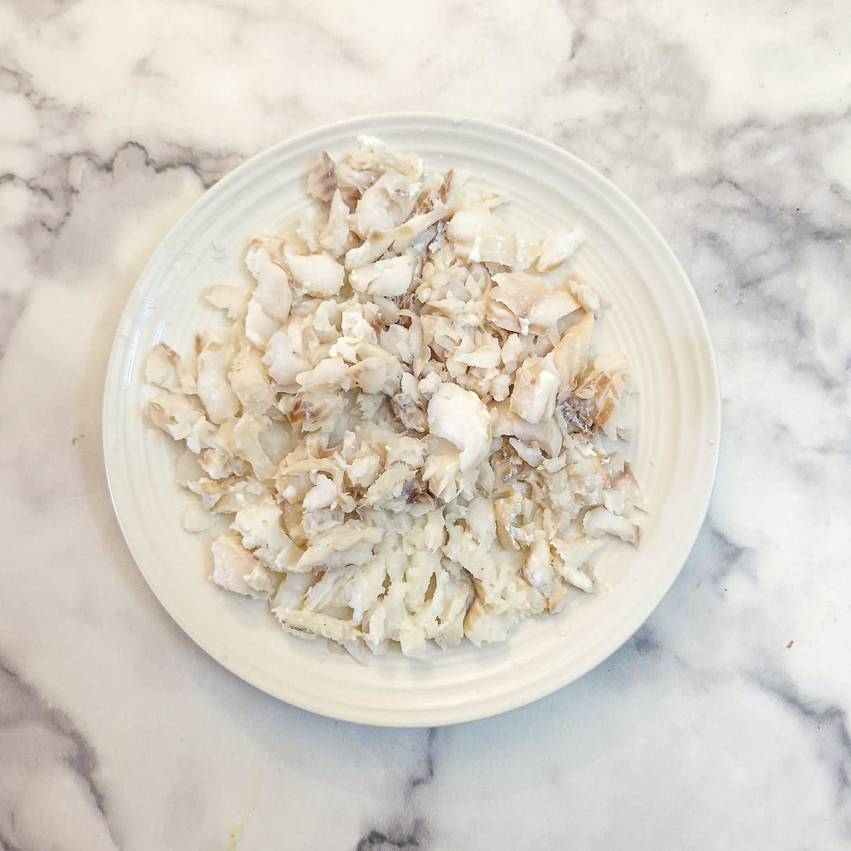 Poached white fish that has been flaked, in a pile on a plate.