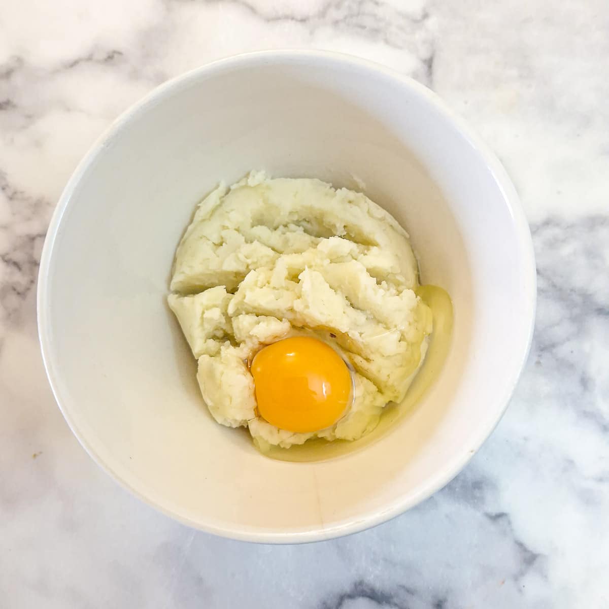 Mashed potatoes in a mixing bowl with an egg.