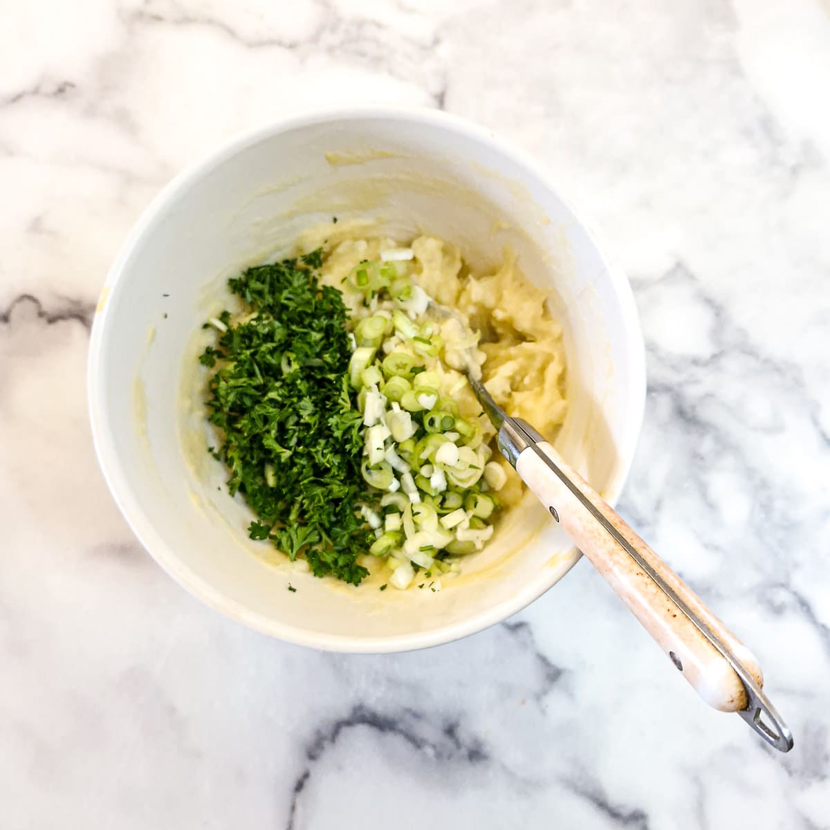 Chopped parsley and spring onions in the bowl of mashed potato and egg.