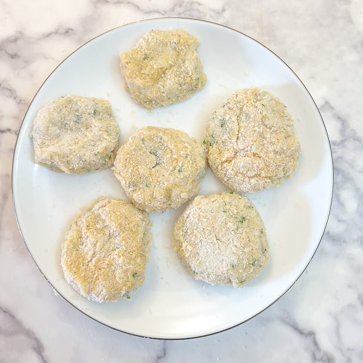 6 coated fish cakes on a white plate.