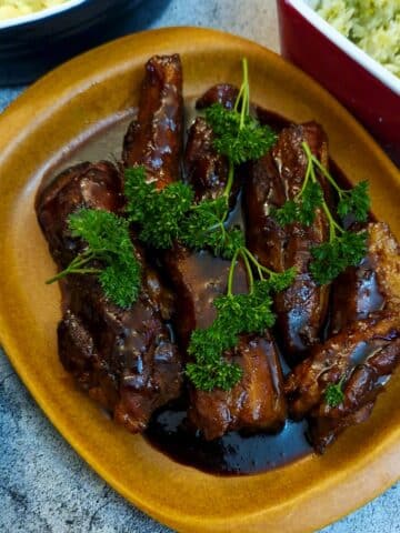 A plate of sticky pork belly rashers, garnished with parslesy and covered with maple glaze, surrounded by vegetable side dishes.
