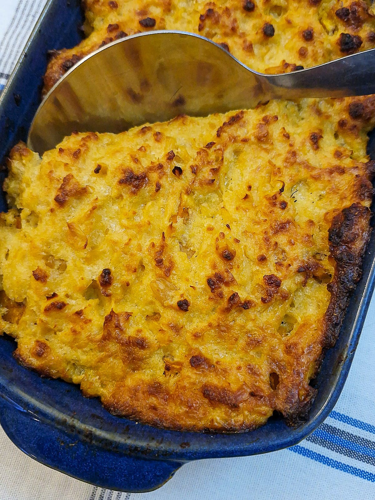 A dish of oven-baked butternut squash with a cheesy corn topping, with a serving spoon.