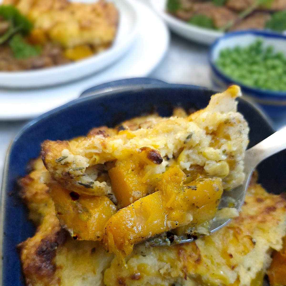 A spoonful of cheesy butternut and corn casserole being lifted from the baking dish.