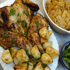 A honey and soy roasted chicken on a serving plate with roast potatoes. There are dishes of vegetables alongside.