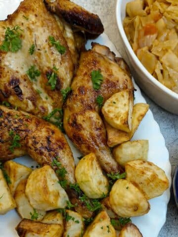 A honey and soy roasted chicken on a serving plate with roast potatoes. There are dishes of vegetables alongside.