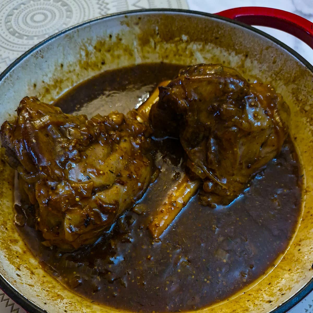 2 lamb shanks in a casserole dish, with lots of gravy.