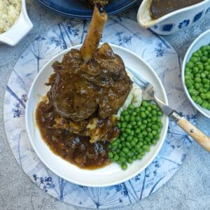 A honey mustard lamb shank on a pile of mustard mash, with a helping of peas on the side.