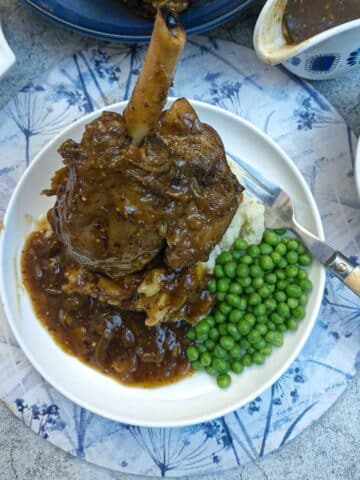 A honey mustard lamb shank on a pile of mustard mash, with a helping of peas on the side.