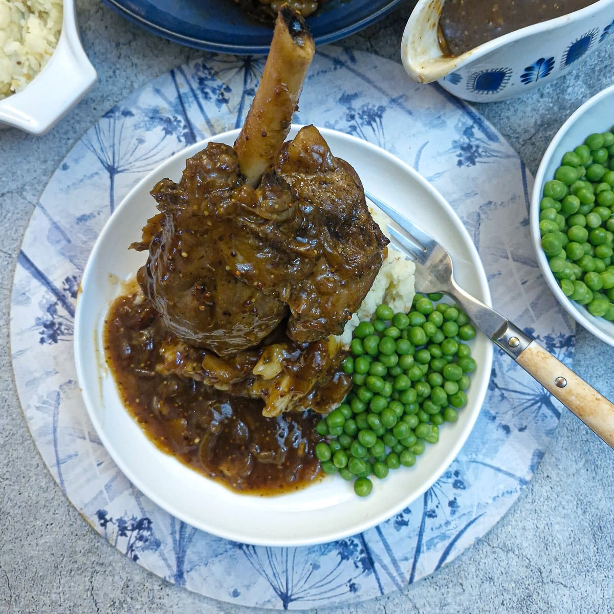 A honey mustard lamb shank on a pile of mustard mash, with a helping of peas on the side.