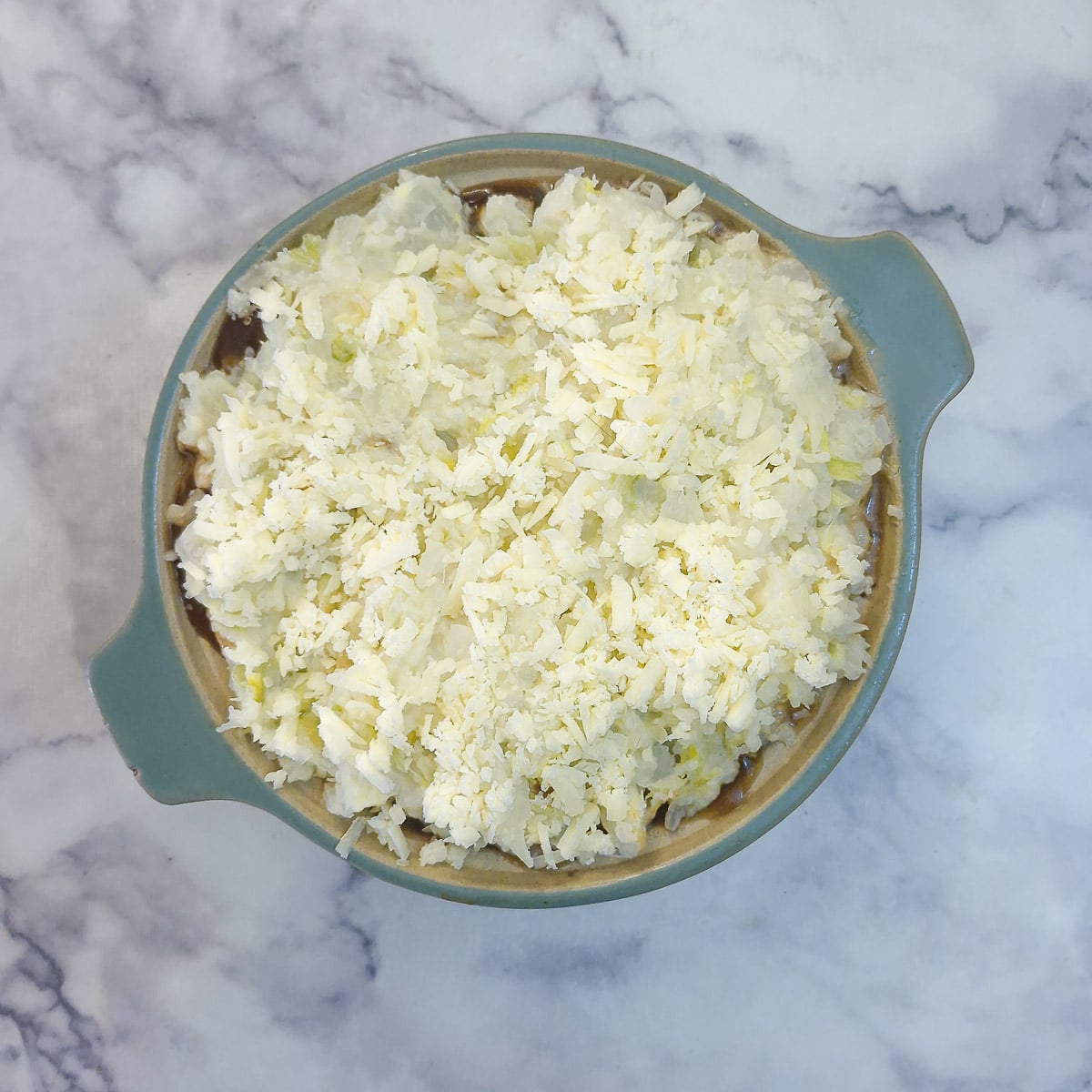 Step 12 - colcannon mash spread over the sausages and sprinkled with grated cheese.
