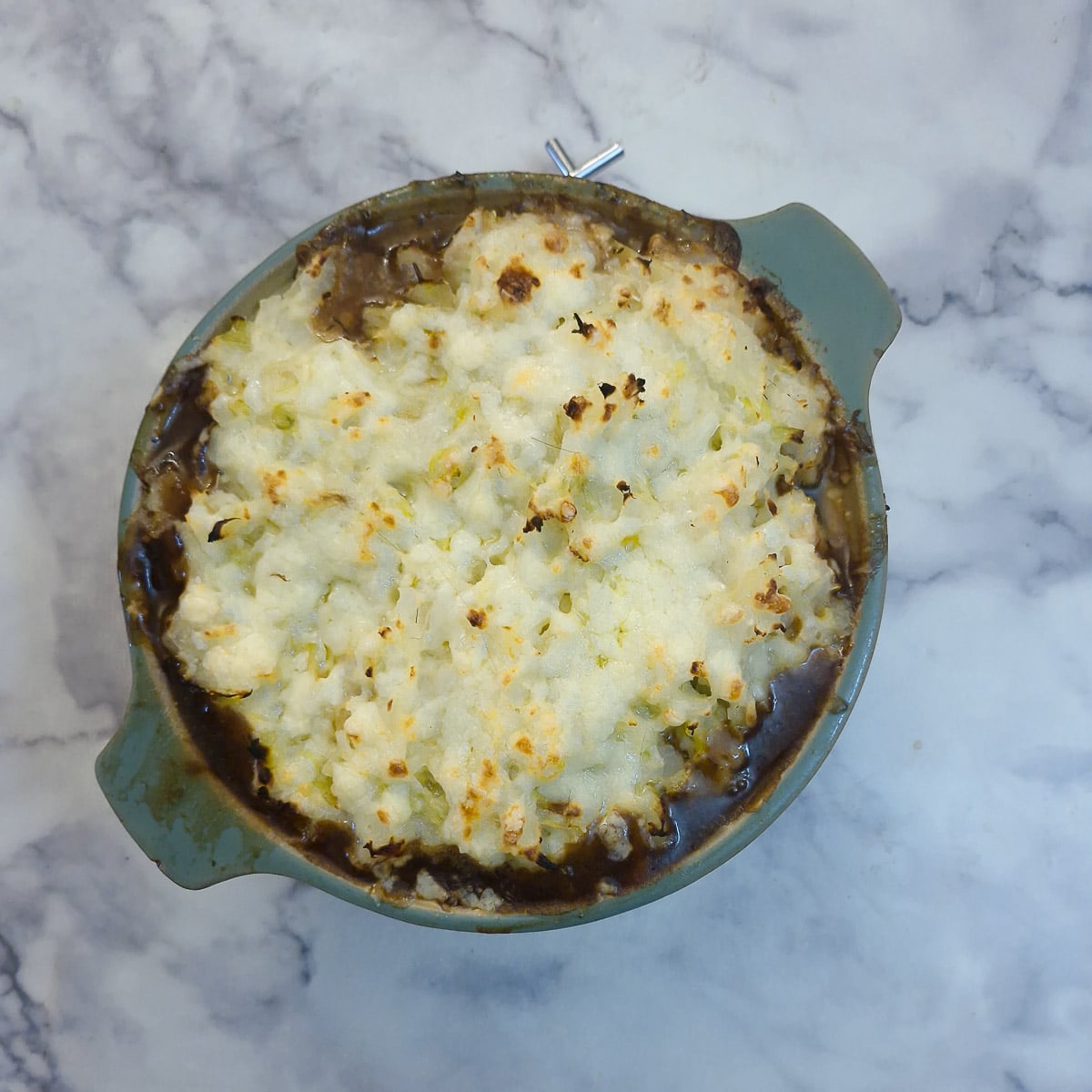 Step 13 - the sausage and onion casserole with a crispy browned colcannon topping in a green casserole dish.