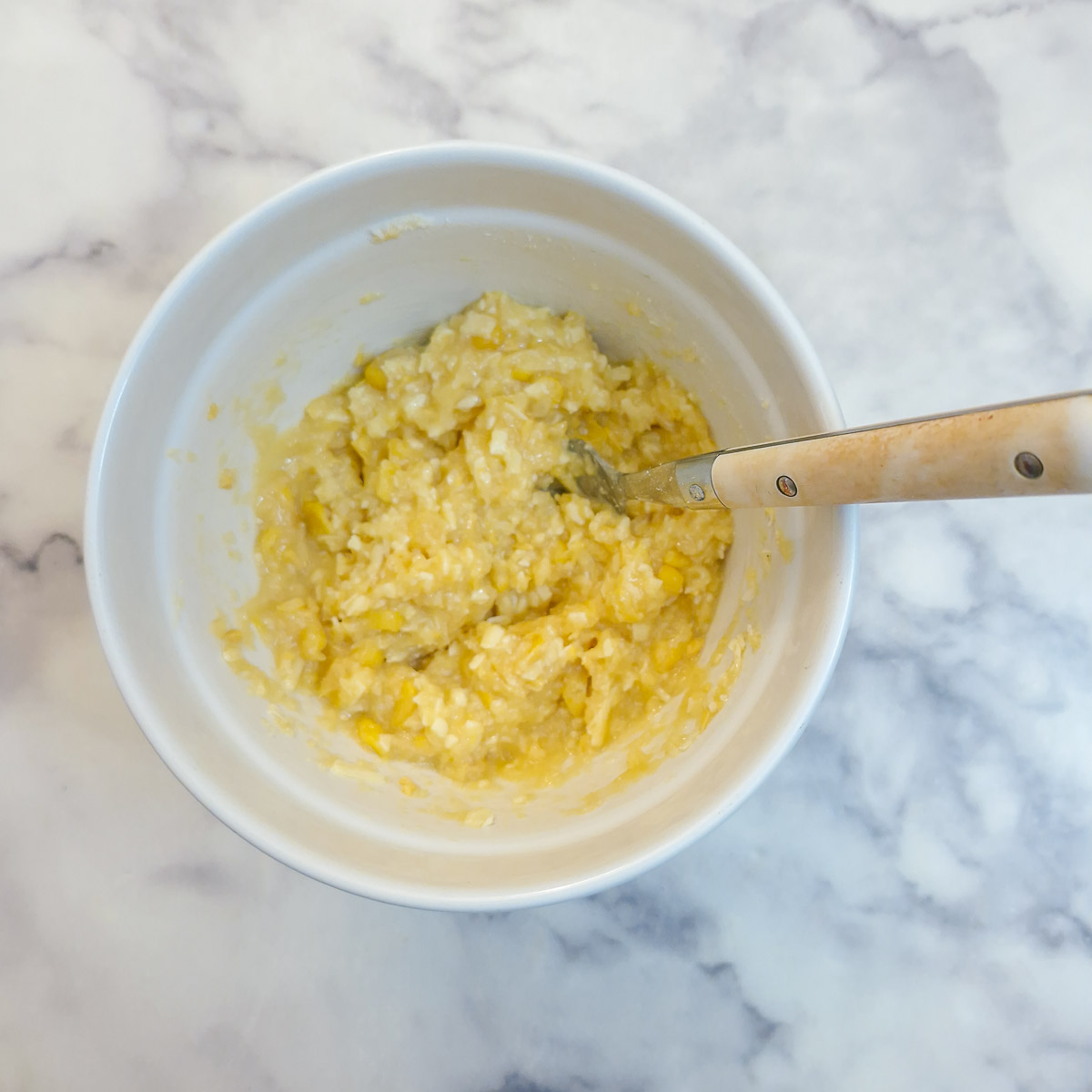 Cheese, breadcrumb and corn topping being combined with an egg in a small mixing bowl.