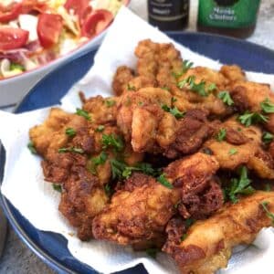 A plate of crispy curried chicken bites alongside a dish of tomato salad.
