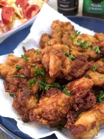 A plate of crispy curried chicken bites alongside a dish of tomato salad.