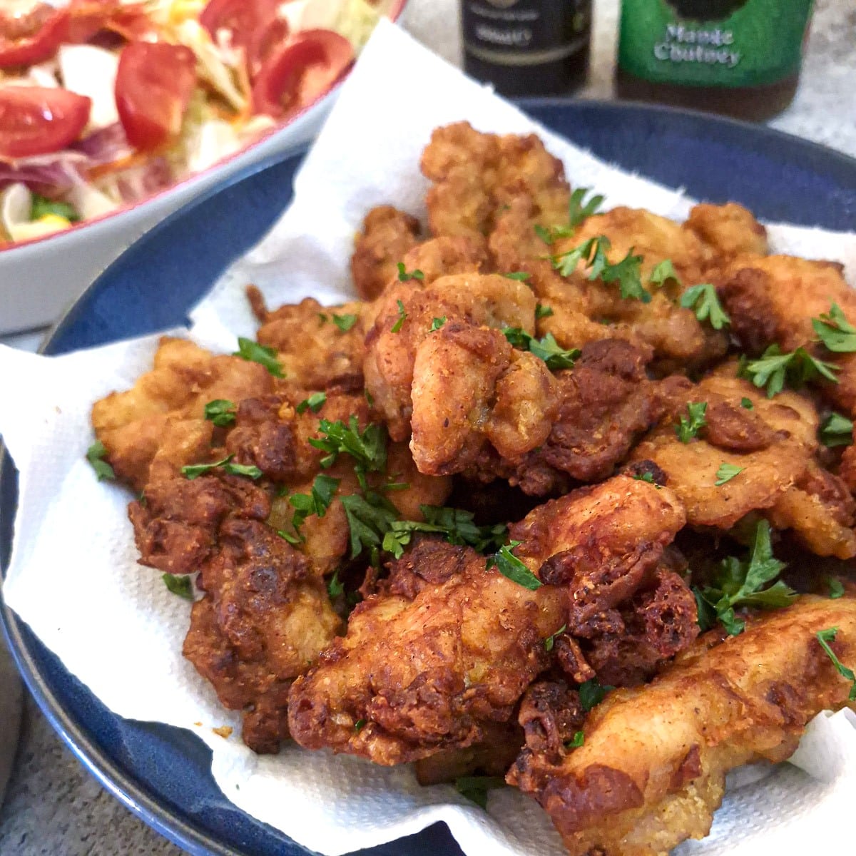 A plate of crispy curried chicken bites alongside a dish of tomato salad.