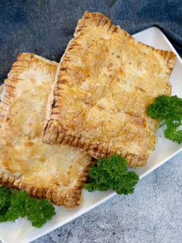 2 Chicken a la king pies in puff pastry on a serving plate, decorated with parsley.