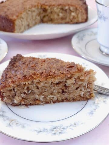 A slice of lemon coconut walnut biscuit cale on a small plate, showing the light crumbly texture. You can clearly see the coconut and pieces of walnuts studded throughout the slice,