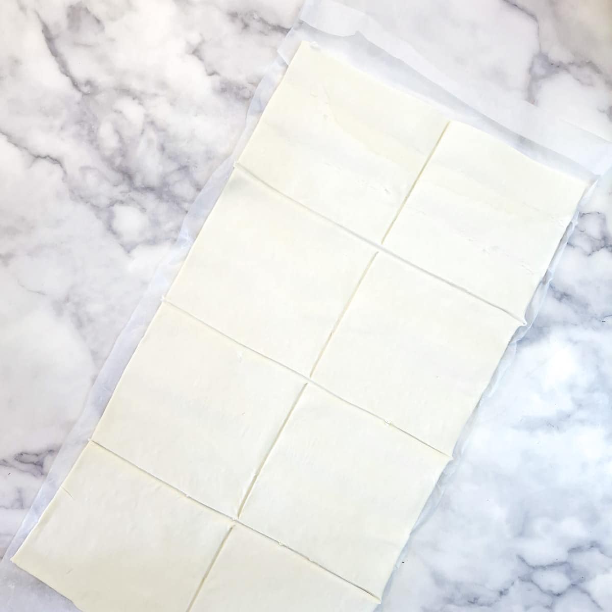 A sheet of unrolled puff pastry cut into 8 squares.