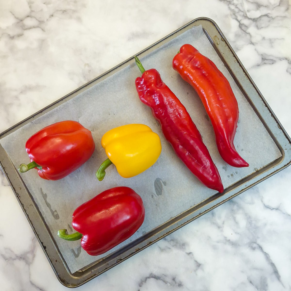 A selection of 5 different peppers on a roasting tray.