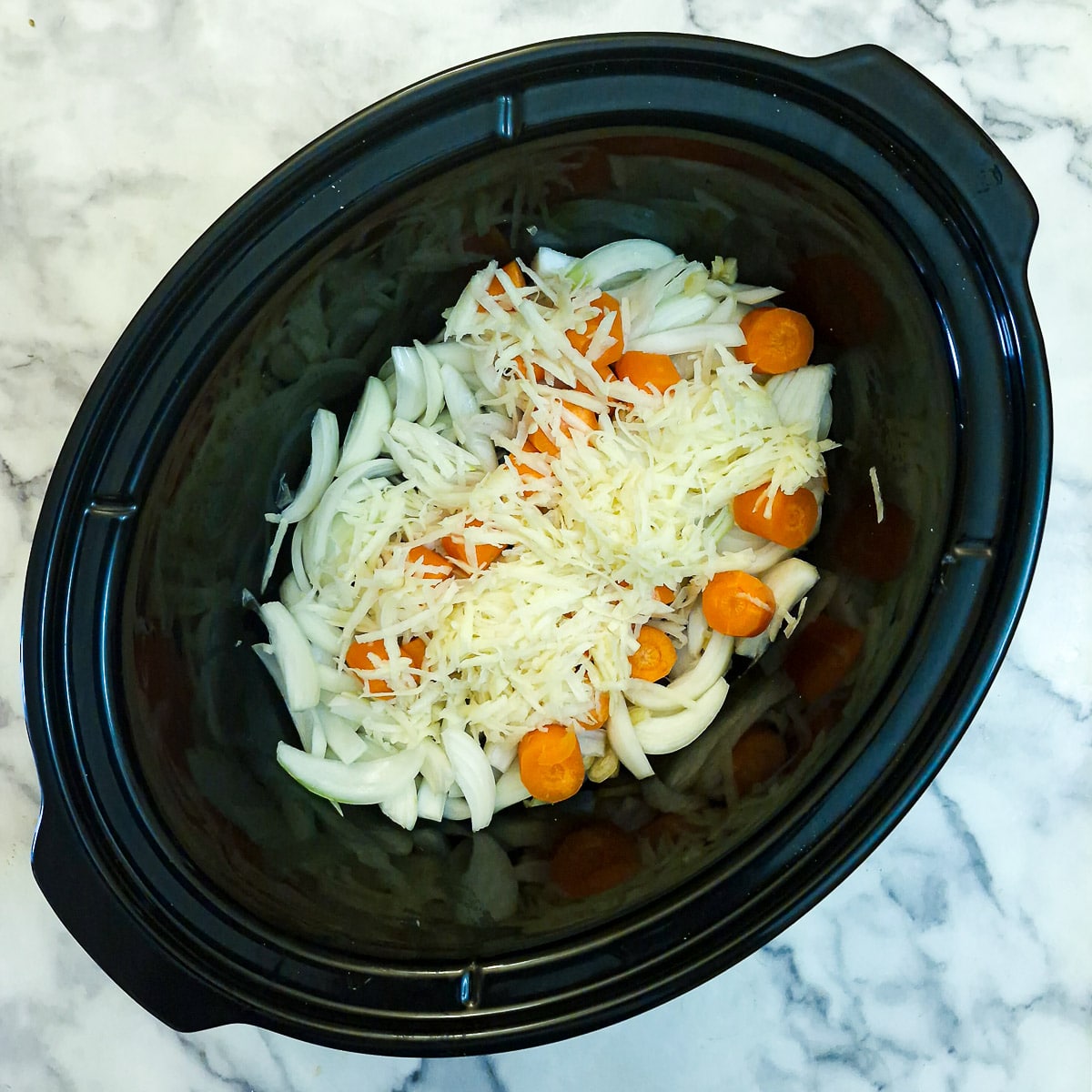 Sliced onions, chunked carrots and grated potatoes in a slow cooker.