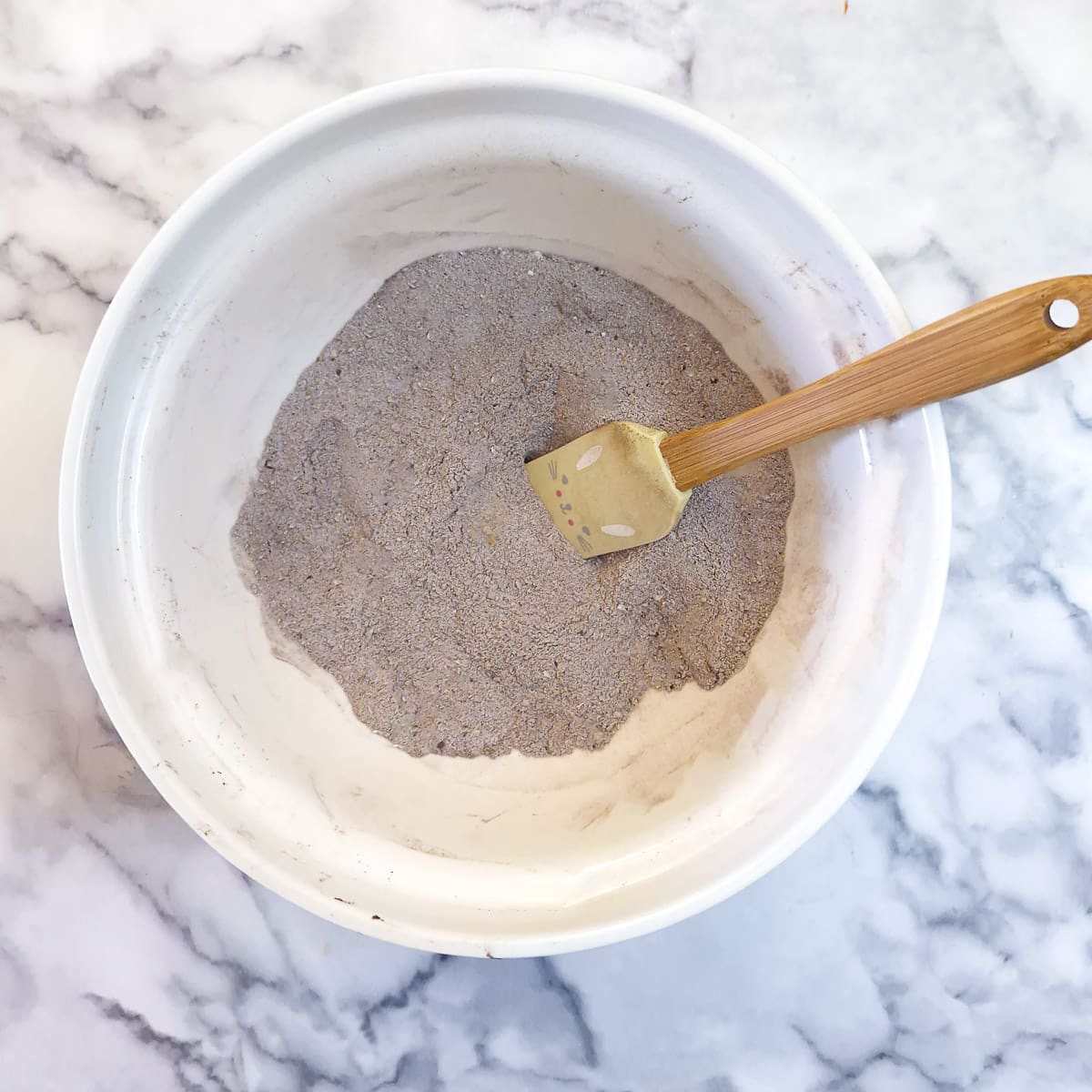 Dry ingredients being combined in a mixing bowl with a spatula.