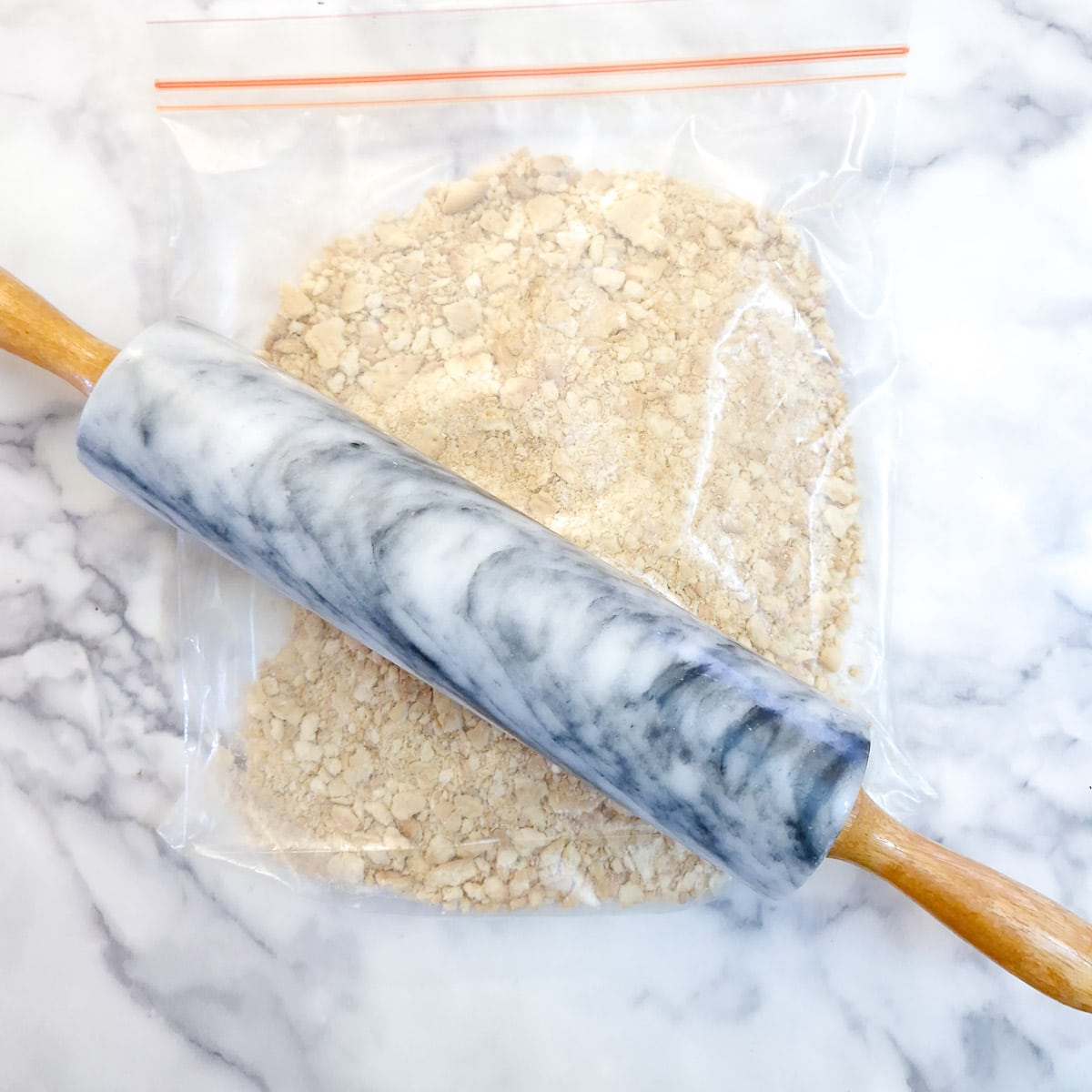 Biscuits being crushed in a plastic bag with a rolling pin.