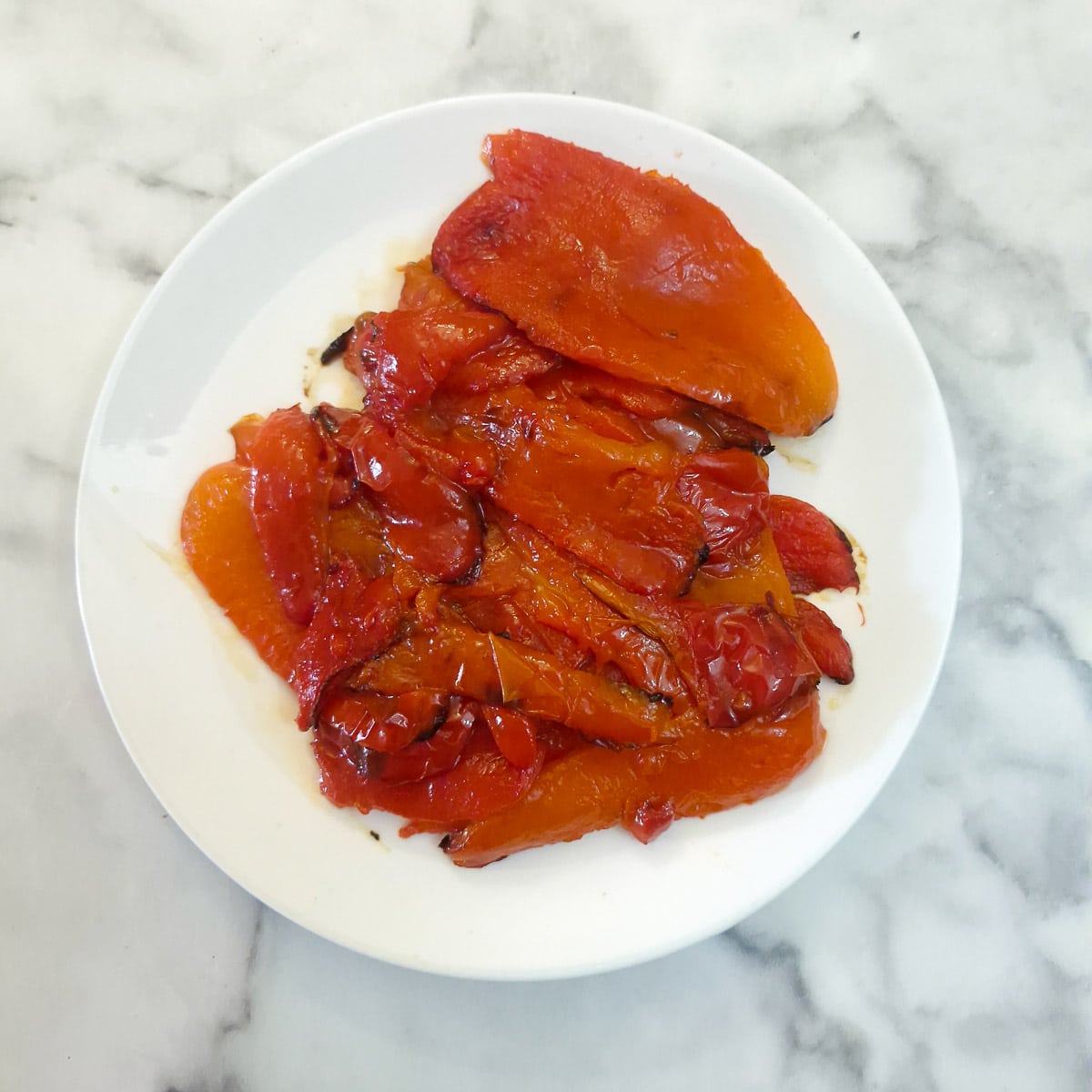 Step 3 - roasted red peppers with the blistered skin removed, on a small white plate.