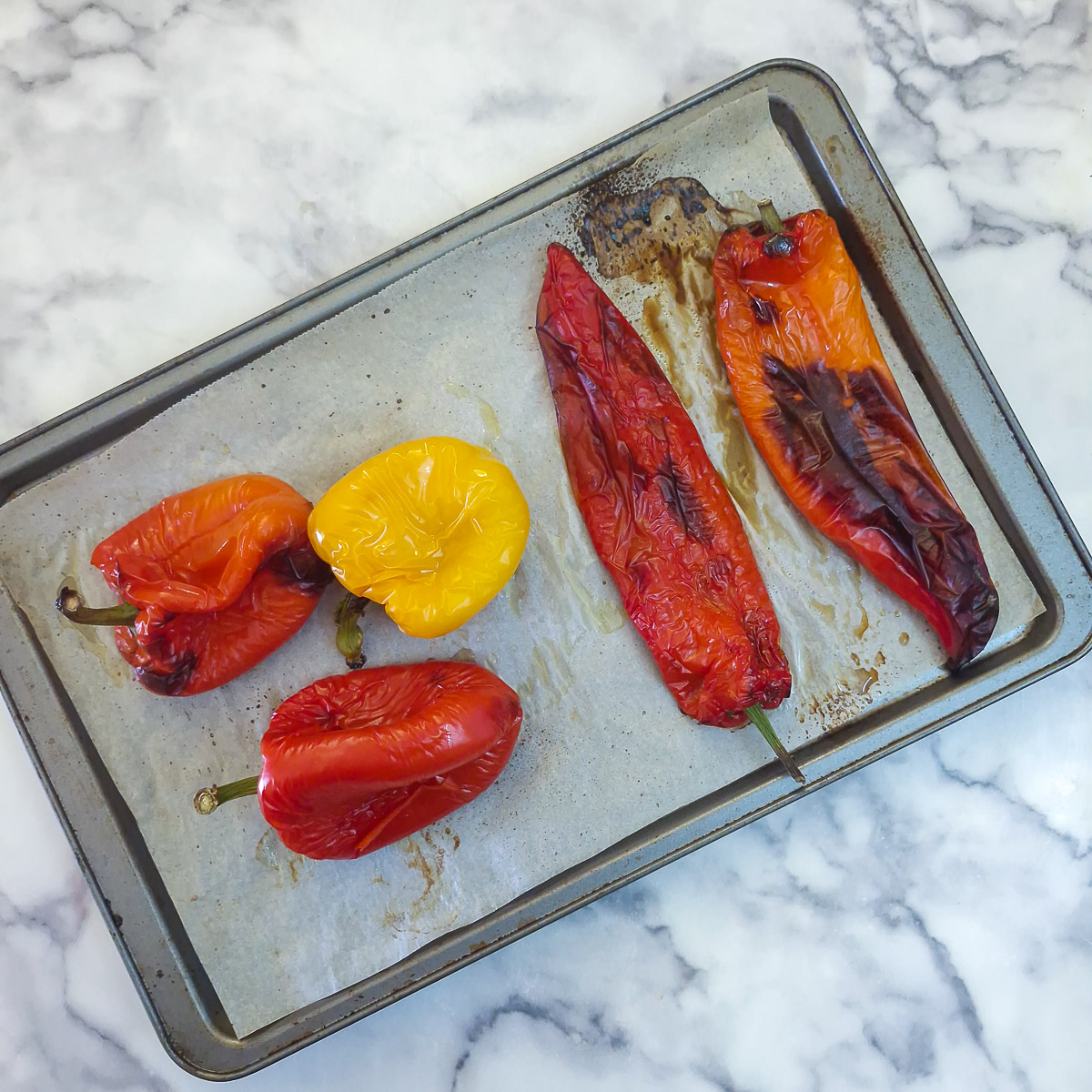 5 peppers on a roasting tray showing how they have charred in the oven.,