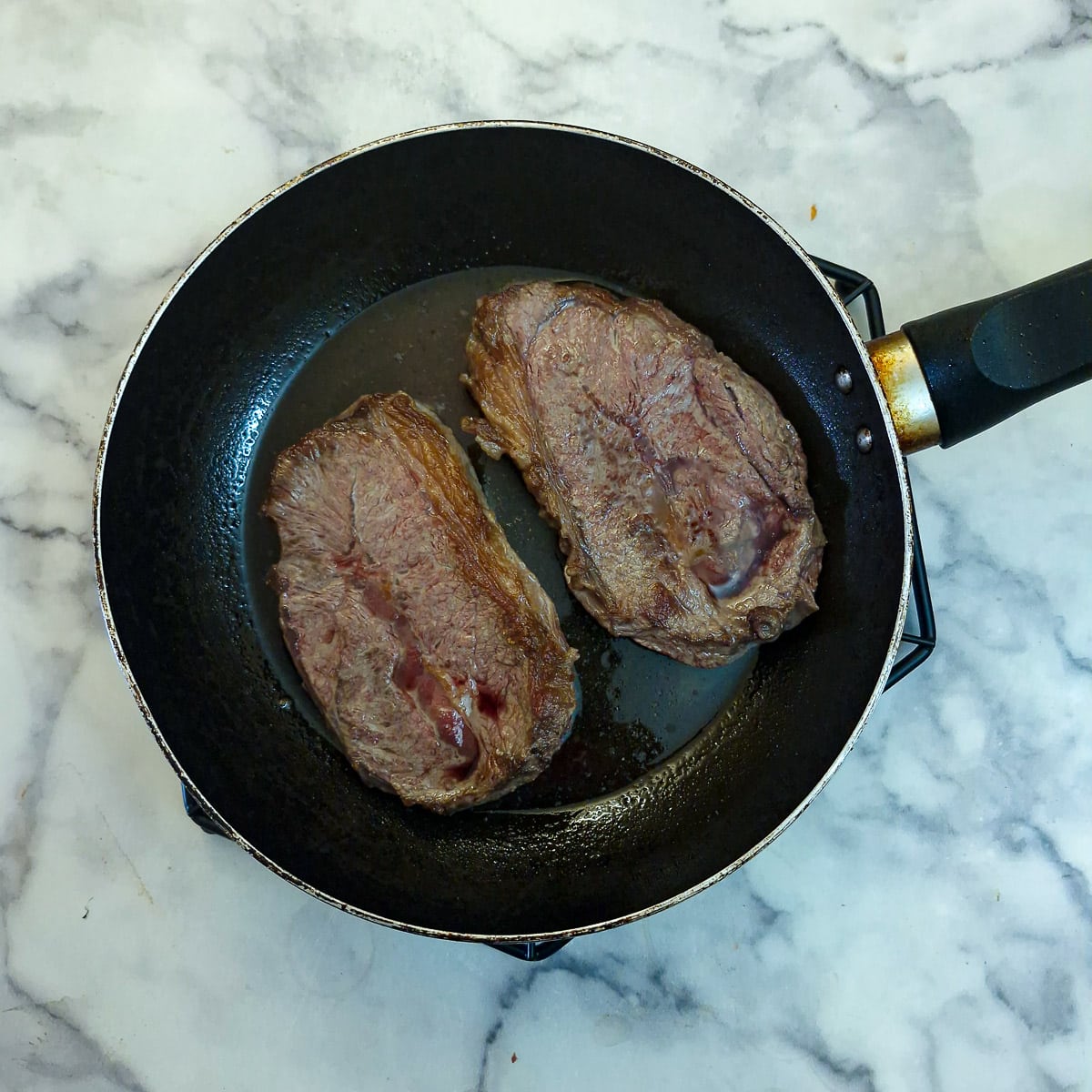 Slices of stewing steak searing in a frying pan.