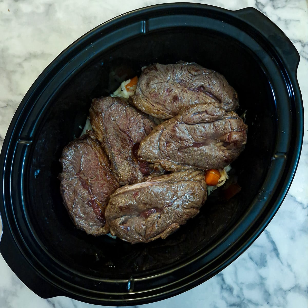 Browned stewing steak arranged on top of the vegetables in the slow cooker.