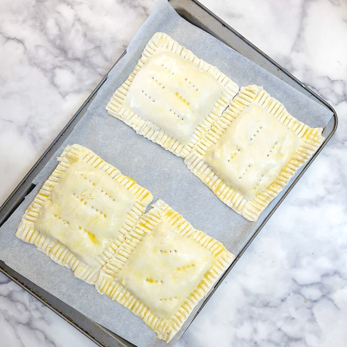 4 fully assembled puff pastry chicken pies on a baking sheet.