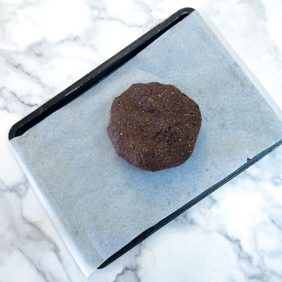 A ball of dough on a baking sheet which has been lined with baking parchment.