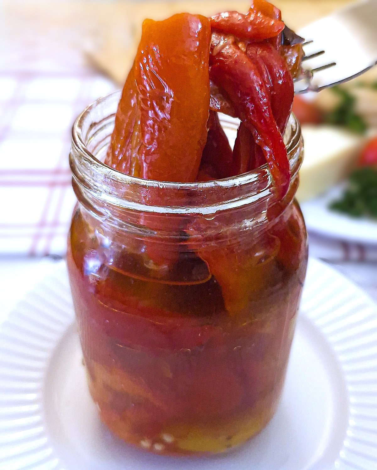 Strips of roasted red peppers being lifted out of the jar with a fork.