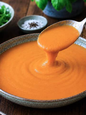 A bowl of roasted red pepper tomato cooking sauce. A largee spoon is being used to lift some of the sauce from the dish.