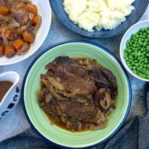A green serving dish filled with slices of slow cooked beef. There are dishes of vegetables surrounding it.