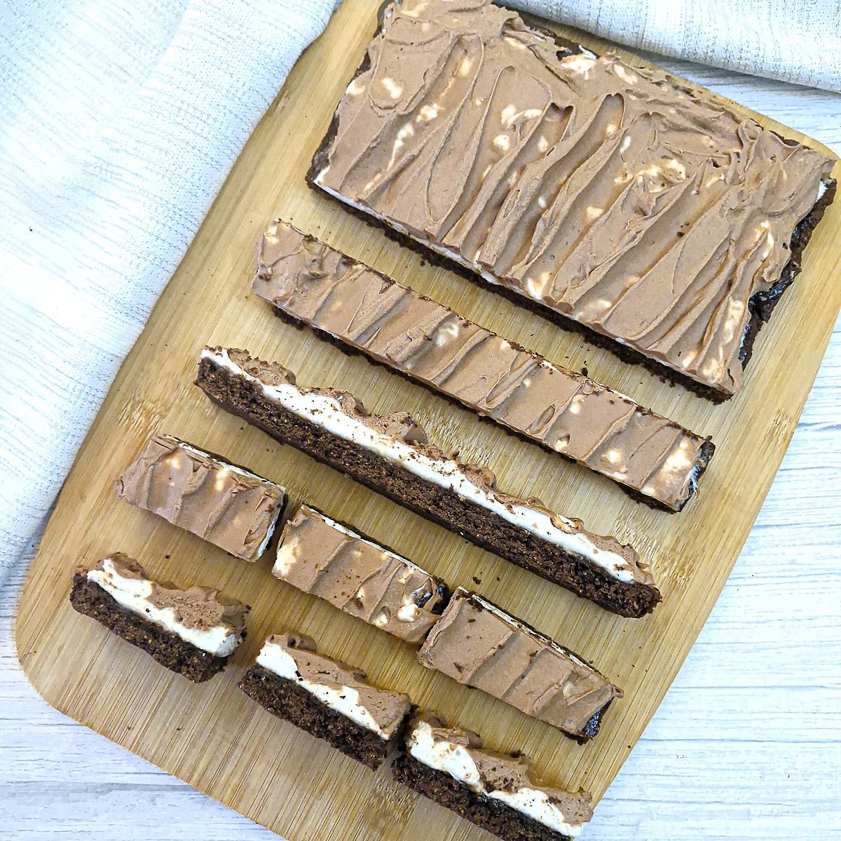 Slices of wagon wheel traybake on a wooden board. Some slices are side on, showing the layers.