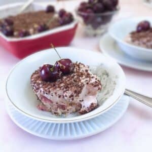 A small dish of milk jelly cherry dessert on a table with the complete serving dish in the background.