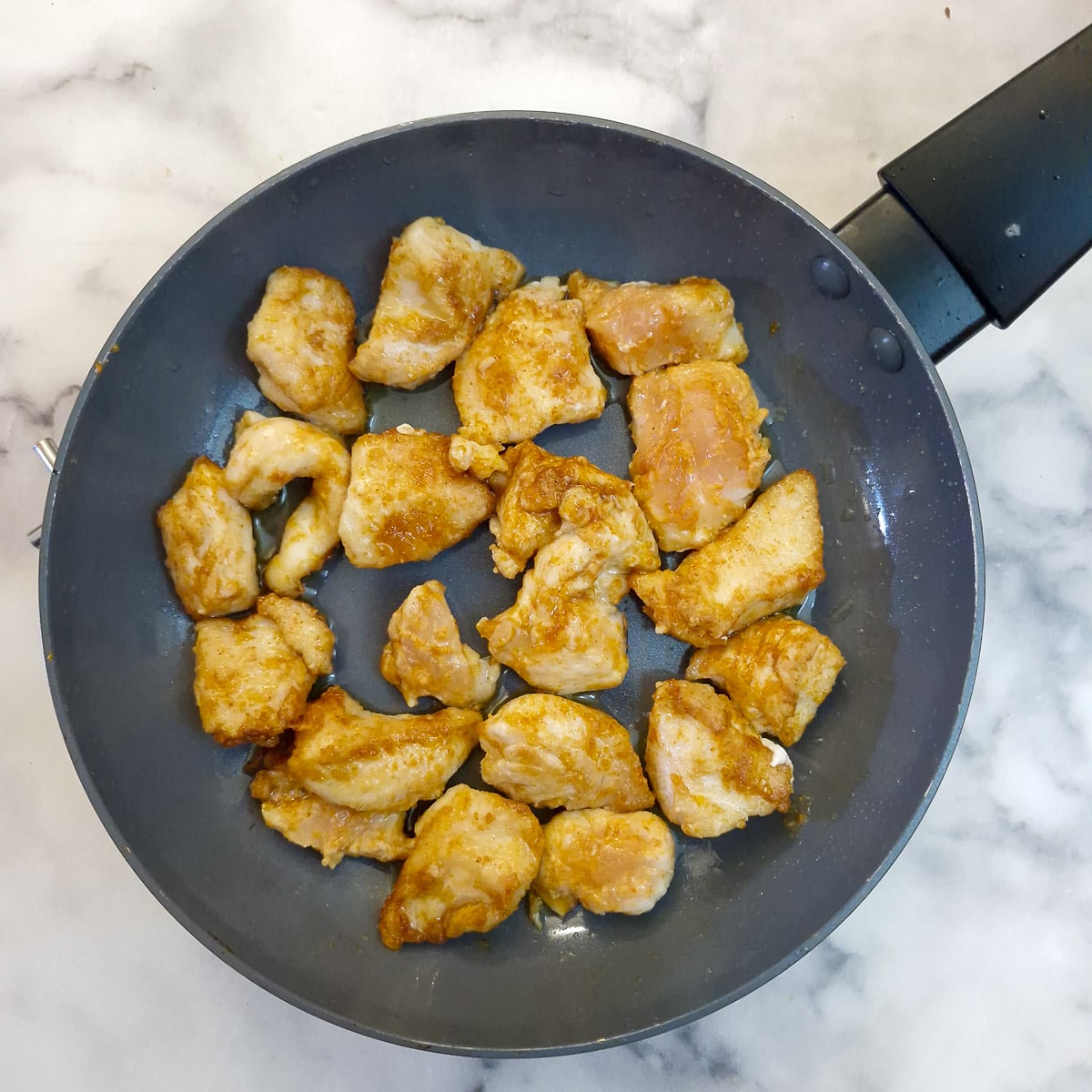 Step 1 - seasoned chicken pieces browning in a frying pan.