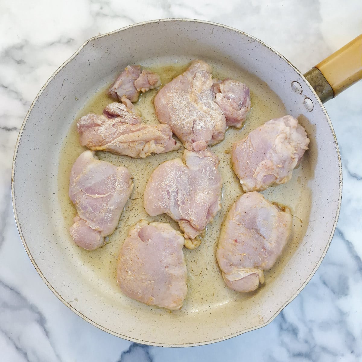Step 1 - Lightly floured chicken thighs placed in a frying pan.