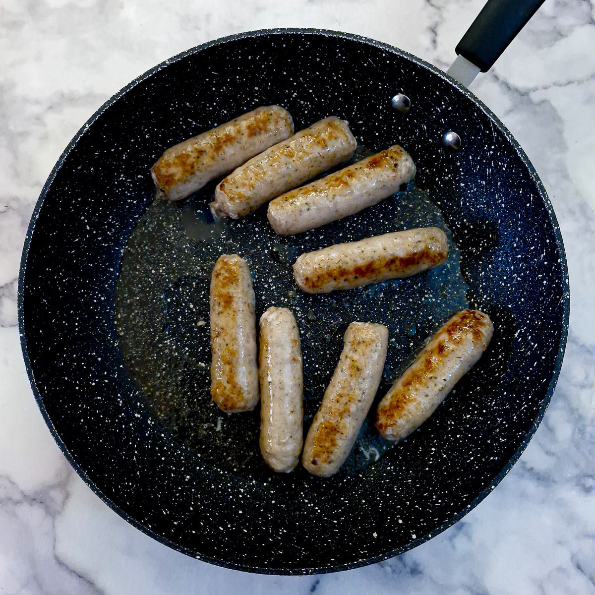 Step 1 - sausages browning in a frying pan.