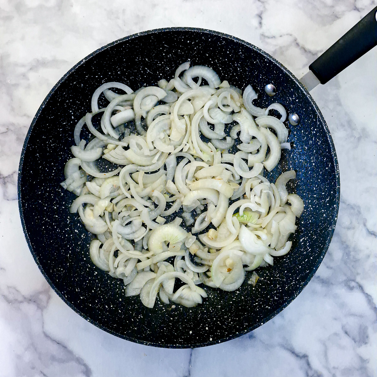 Step 2 - sliced onions softening in a frying pan.