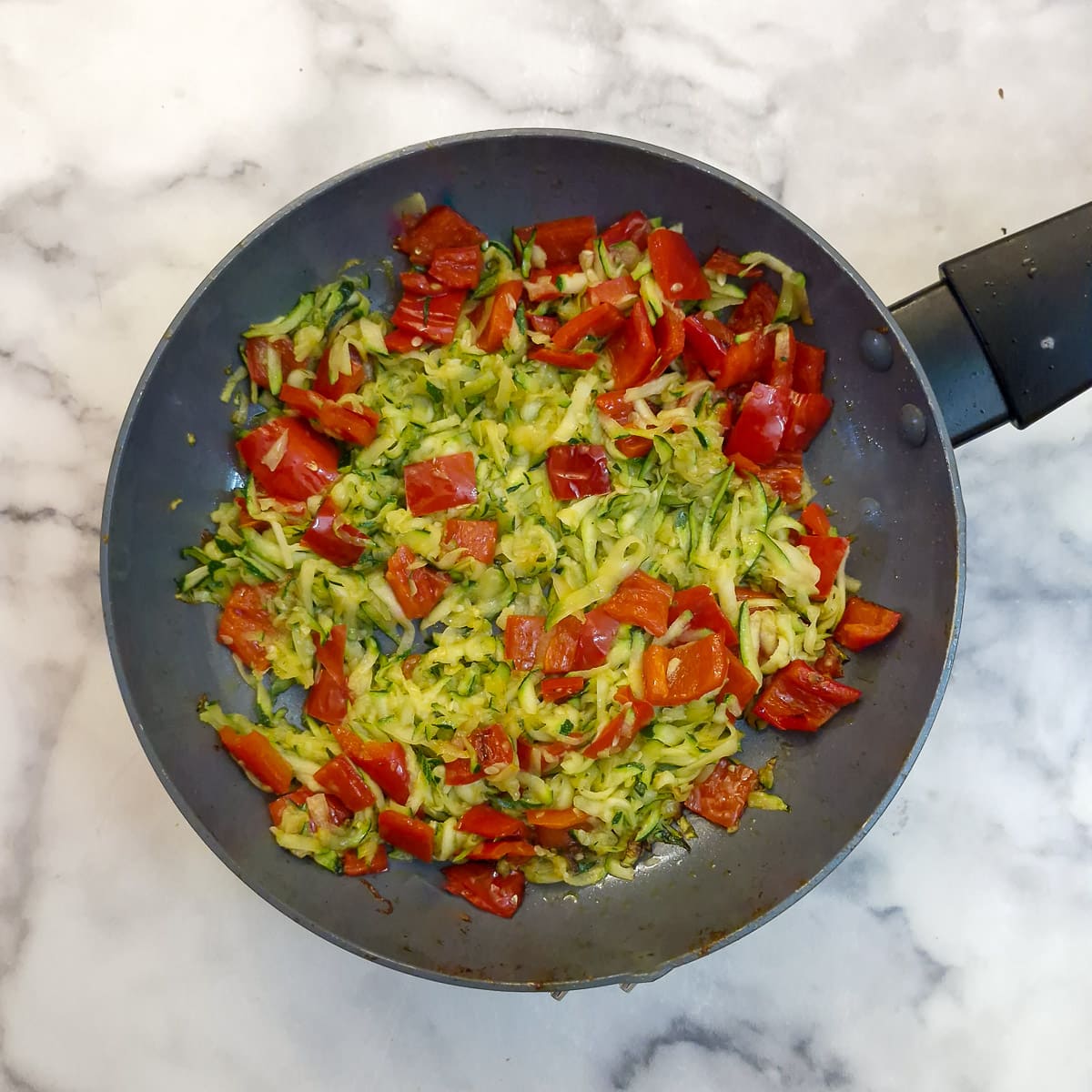 Step 5 - grated courgettes added to the red peppers in a frying pan.