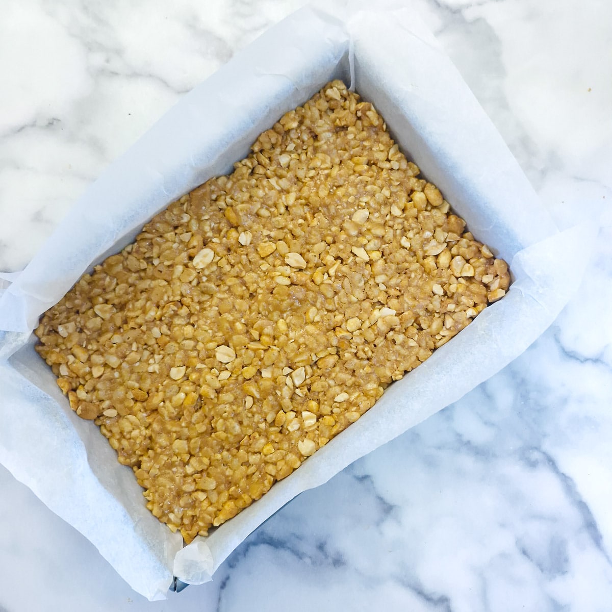 Step 5 - The peanut and rice cereal mixture pressed into a lined baking pan.