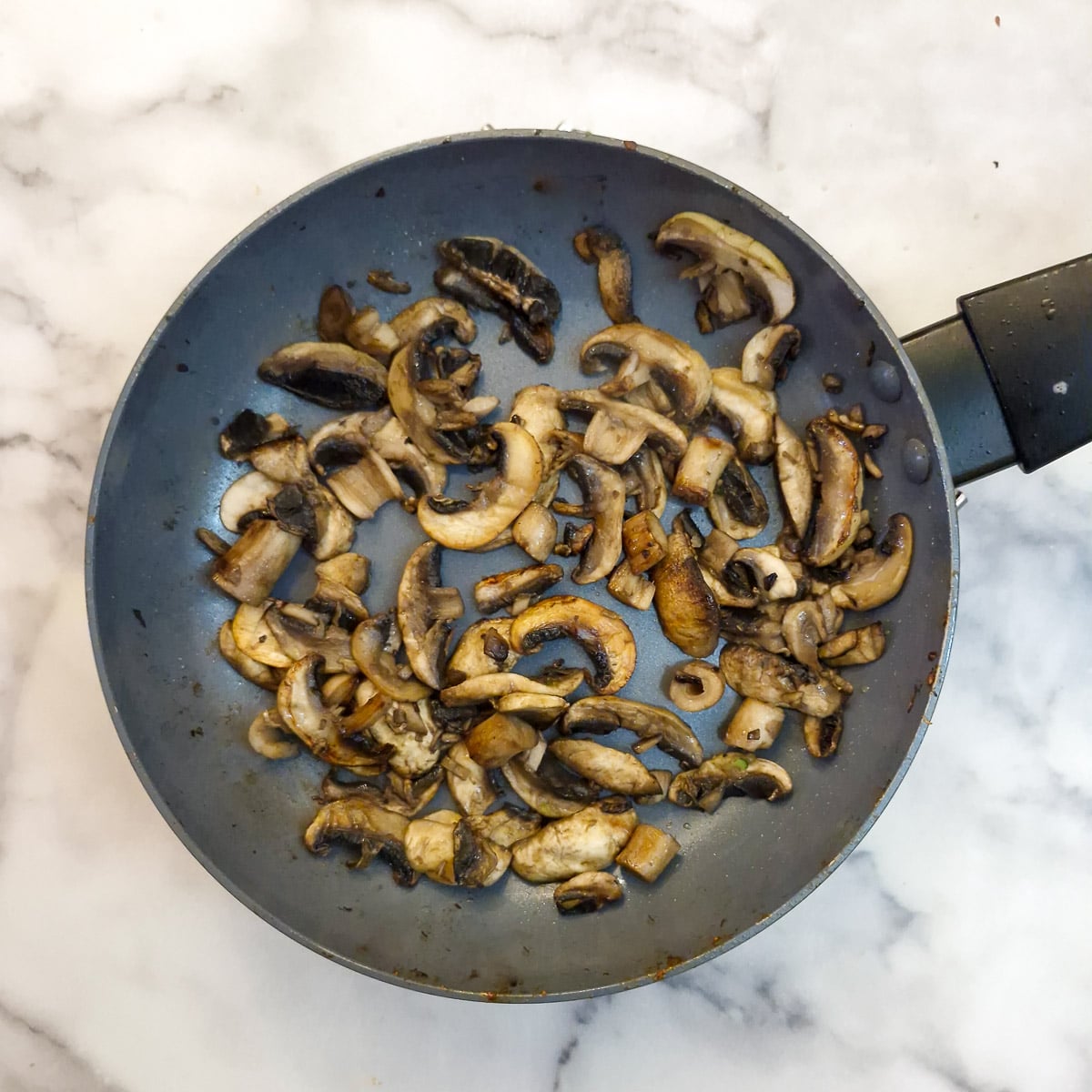 Step 7 - sliced mushrooms softening in a frying pan.