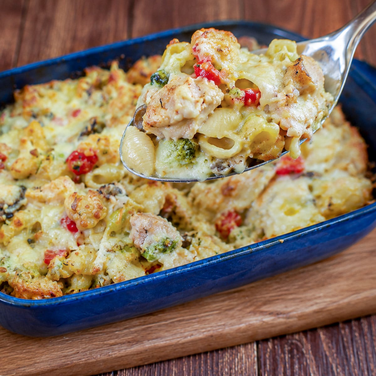 A large spoonful of chicken pasta bake being lifted from the casserole dish.