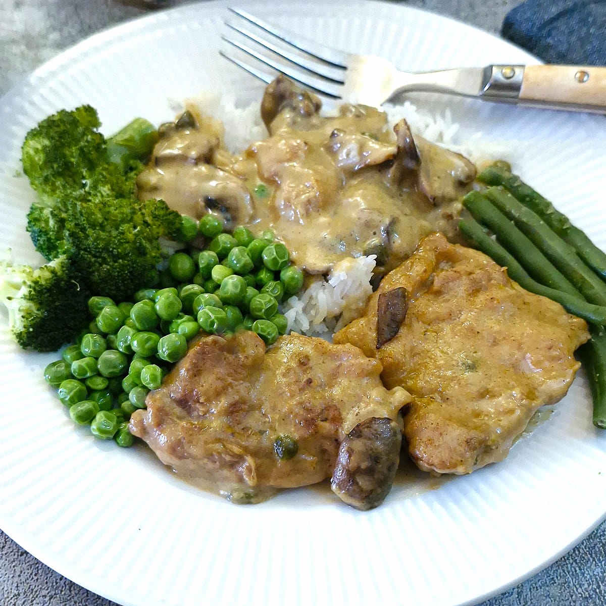 Two pieces of chicken marsala on a plate with rice and green vegetables. There is plenty of marsala sauce covering the rice.