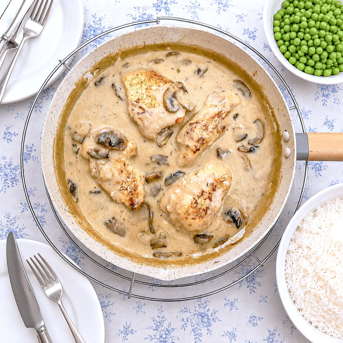 A dish of creamy chicken masala on a table with a dish of peas and a dish of rice.
