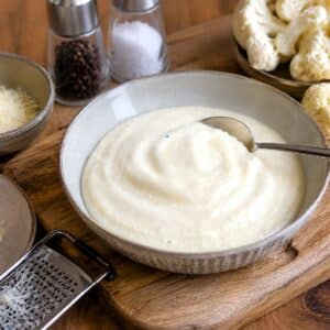 Ceamy parmesan cauliflower sauce in a light grey bowl with a spoon.