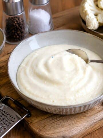 Ceamy parmesan cauliflower sauce in a light grey bowl with a spoon.